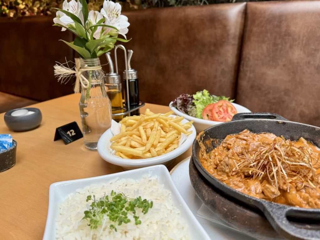 Mesa de restaurante com pratos de comida servindo um strognoff com batata frita